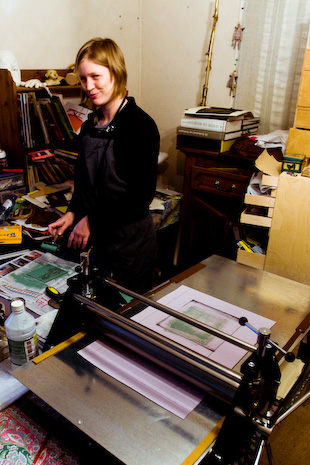 kunstenaares Steph Heyvaert is langs de drukpers een linoleumsnede aan het instrijken om te drukken