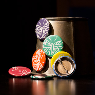 een aantal magneten op een ijzeren emmertje, vooraan een opspeldbutton, allemaal vlinderdesigns in verschillende kleuren