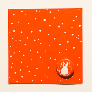 een Kerstkaart, een kaart met witte sneeuwvlokjes op een rode achtergrond voorzien van een opgespelde button met een pinguïn