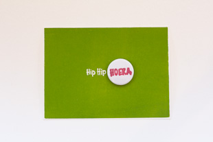 een groen verjaardagskaartje met een pin waar HOERA op staat in het paars